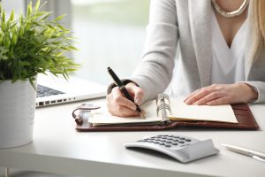 Close-up of businesswoman holding pen in hands and writing a note.