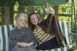 The girl sitting in the hammock with grandma and makes selfie.