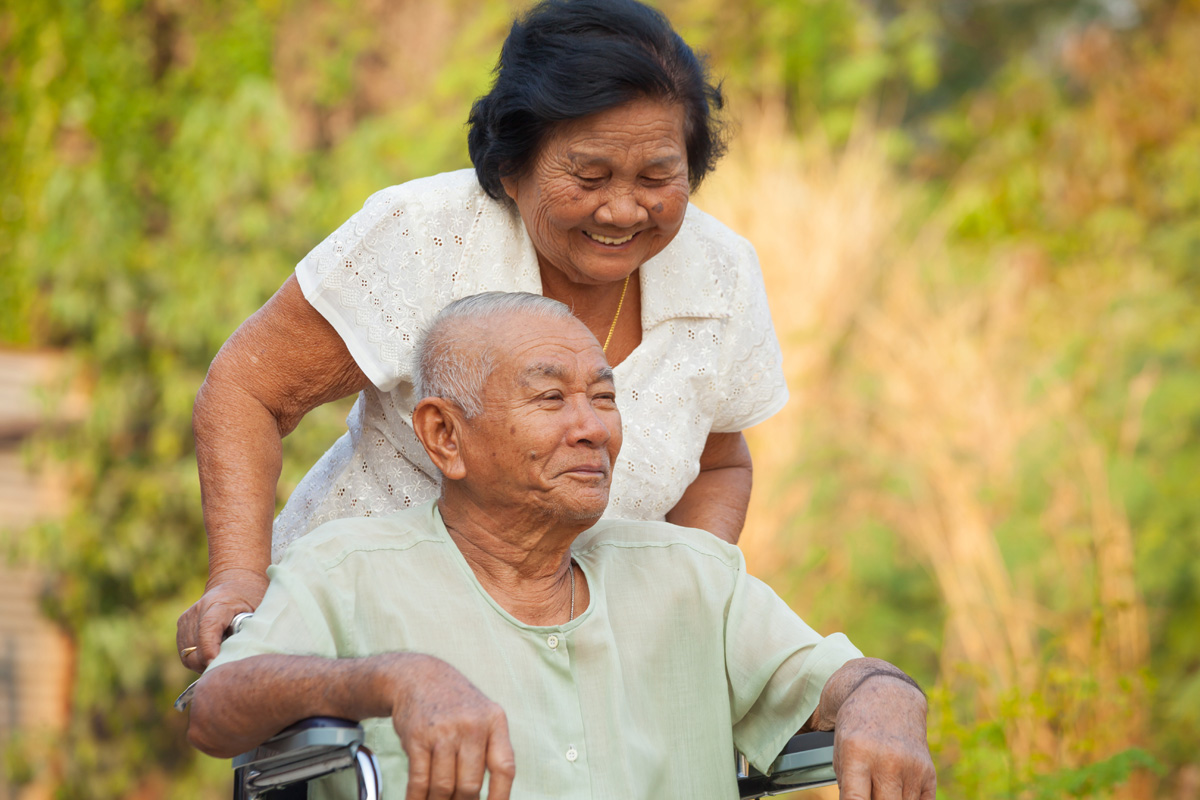 Asian senior woman pushing her disabled hasband on wheelchair